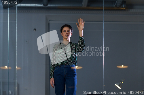 Image of businesswoman using glass wall at night office