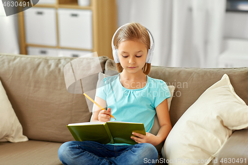 Image of girl in headphones with diary on sofa at home