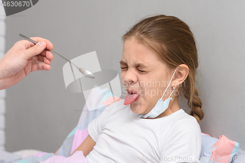 Image of The girl frowns at the medicine given to her and pulled out her tongue