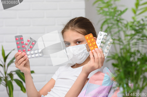 Image of Girl holding in her hands a lot of pills in a pack, even in a medical mask in bed
