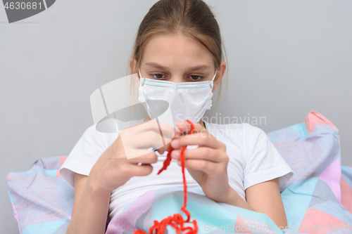 Image of Ill girl in a medical mask knits lying in bed
