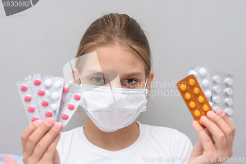 Image of A girl with a medical mask on her face holds blisters with medicines