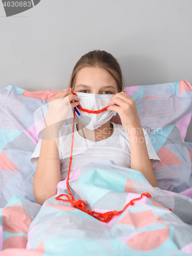 Image of A girl in a medical mask in quarantine knits and made a smile out of thread on the mask