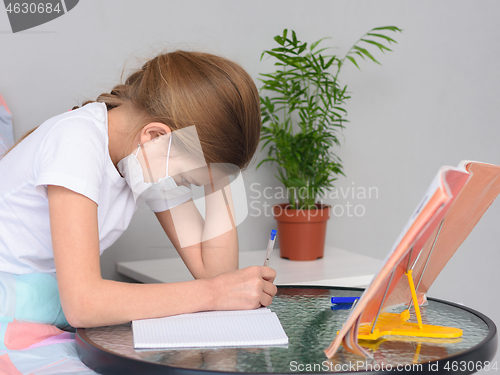 Image of A girl in a medical mask does homework at a table in front of the bed