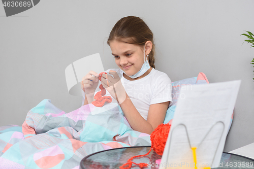 Image of The sick girl in quarantine at home is engaged in needlework lying in bed.