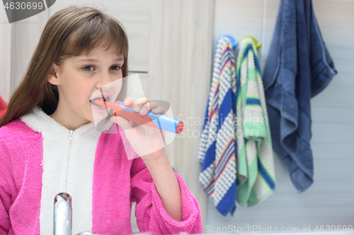 Image of Ten year old girl brushes her teeth with an electric toothbrush in the bathroom