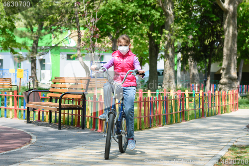Image of A ten-year-old girl in a medical protective mask rides a Bicycle