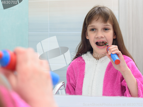 Image of The girl looks in the mirror and brushes her teeth with an electric toothbrush