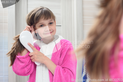 Image of Happy girl combing hair in the bathroom