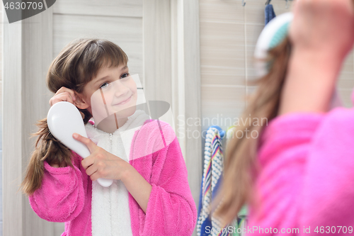 Image of Happy girl combing long hair looks and looks in the mirror