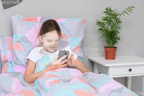 Image of Girl communicates with friends online in a mobile phone while lying in bed.