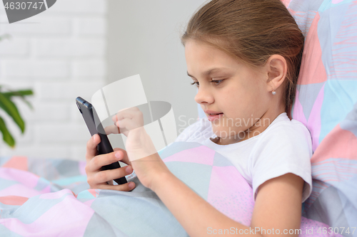 Image of The girl lies in bed and plays in a mobile smartphone