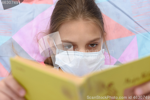 Image of Girl in a medical mask reads a book while lying in bed, close-up