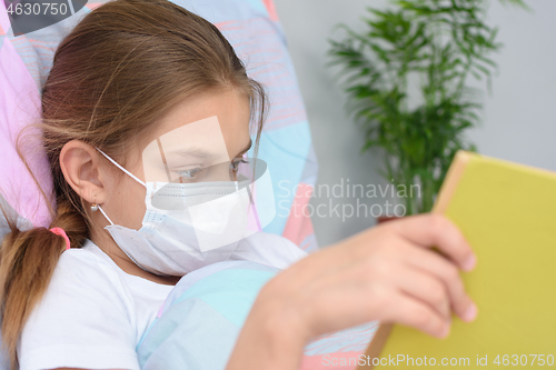 Image of Girl reading a book while lying in bed in a hospital ward