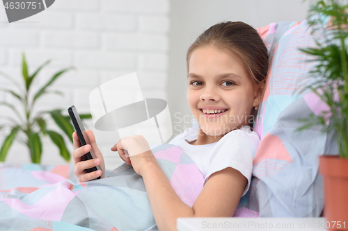 Image of The girl plays in the mobile phone and looked happily into the frame.