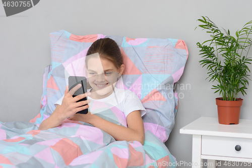 Image of Happy girl lying in bed communicates on a mobile phone