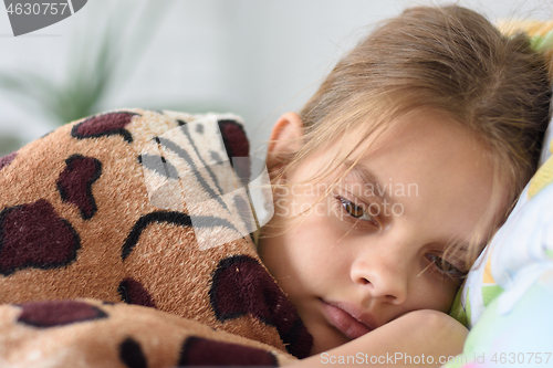 Image of Girl slowly wakes up, lying in bed and covered with an old blanket
