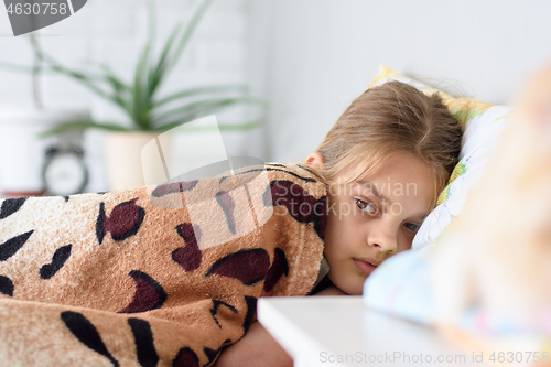Image of Girl lying in bed covered with an old bedspread