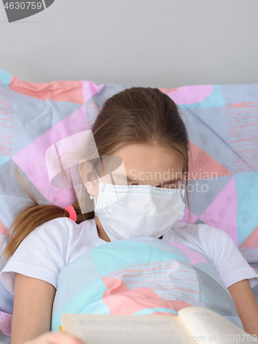 Image of The sick girl decided to fall asleep while reading a book and pulled a medical mask over her face