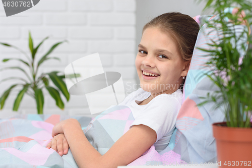 Image of Happy ten-year-old girl in the morning lies in bed and smiles into the frame.