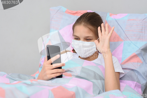 Image of A sick girl lies in bed and communicates with friends online via video-telephone