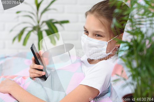 Image of A recovering quarantined girl smiles and holds a mobile phone in her hands