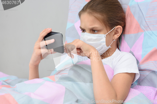 Image of The quarantined girl lies in bed with a mobile phone