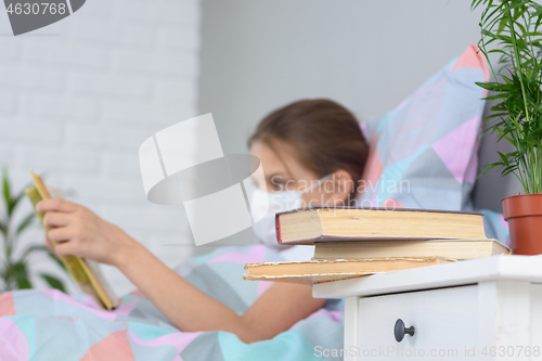 Image of A girl with influenza is reading a book, books are on the nightstand in front of her, focusing on books