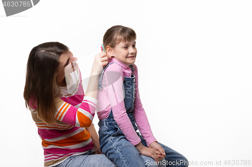 Image of Girl sitting on moms lap, mom fun tugs at the girls ear