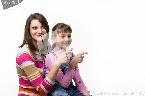 Image of Girl sitting on moms lap and joyfully point a finger to an empty place