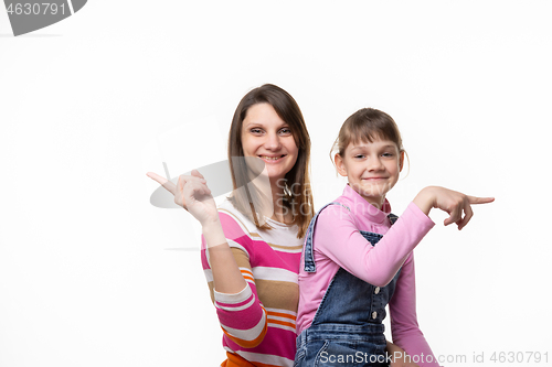 Image of Cheerful mother and daughter point fingers in different directions, isolated on white background