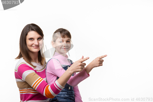 Image of A girl sits on her mothers lap and joyfully points a finger at an empty place, looks into the frame
