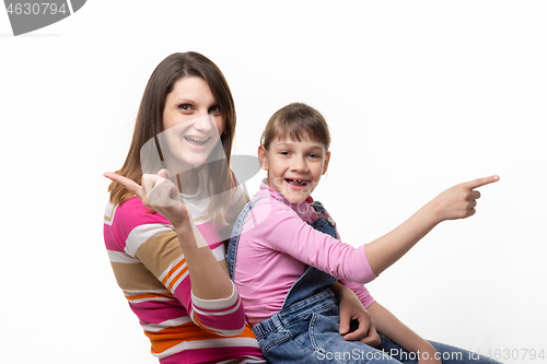 Image of Joyful mom and daughter point finger in different directions, isolated on white background