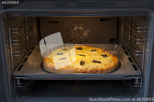 Image of Baking quattro formaggi pizza in oven with open door.