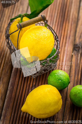 Image of Organic lemons and limes in a basket on wooden background