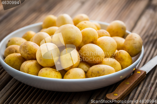 Image of Fresh organic small potatoes in bowl with knife on wooden background