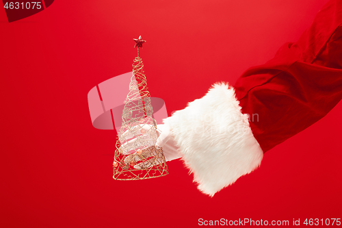 Image of Hand of Santa Claus holding a toy christmas tree on red background