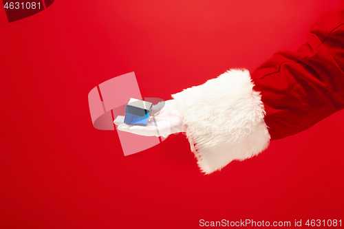 Image of Hand of Santa Claus holding a gift on red background