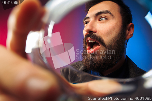 Image of The surprised young man in party clothes posing with glass of wine.