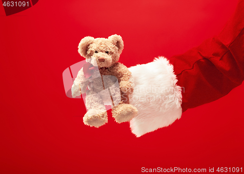 Image of Hand of Santa Claus holding a gift on red background