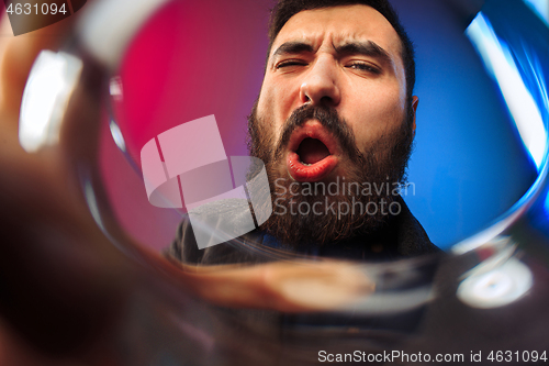 Image of The surprised young man in party clothes posing with glass of wine.