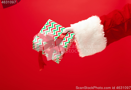 Image of Hand of Santa Claus holding a gift on red background