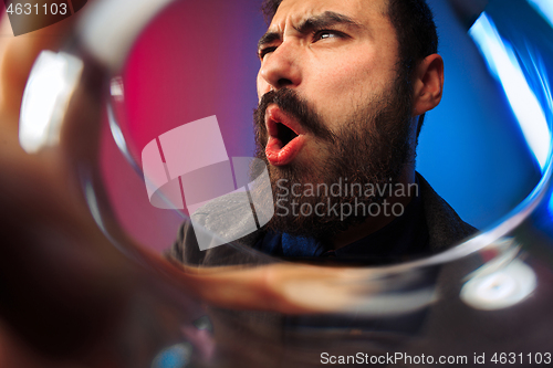 Image of The surprised young man in party clothes posing with glass of wine.