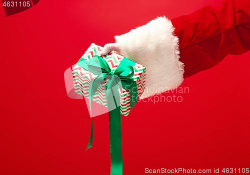 Image of Hand of Santa Claus holding a gift on red background