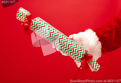 Image of Hand of Santa Claus holding a gift on red background