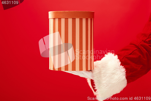 Image of Hand of Santa Claus holding a gift on red background