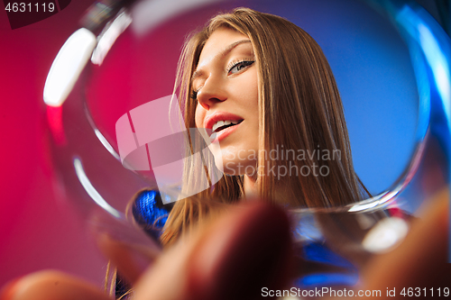 Image of The surprised young woman in party clothes posing with glass of wine.