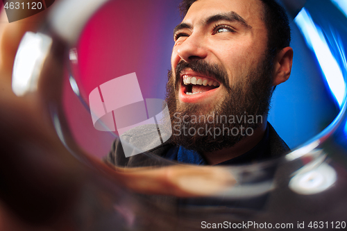 Image of The surprised young man in party clothes posing with glass of wine.