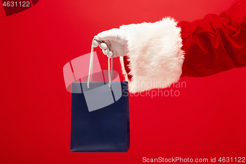 Image of Hand of Santa Claus holding a gift on red background