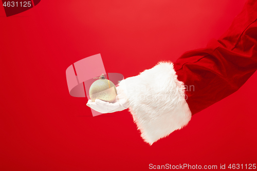 Image of Hand of Santa Claus holding a toy Christmas decorations on red background